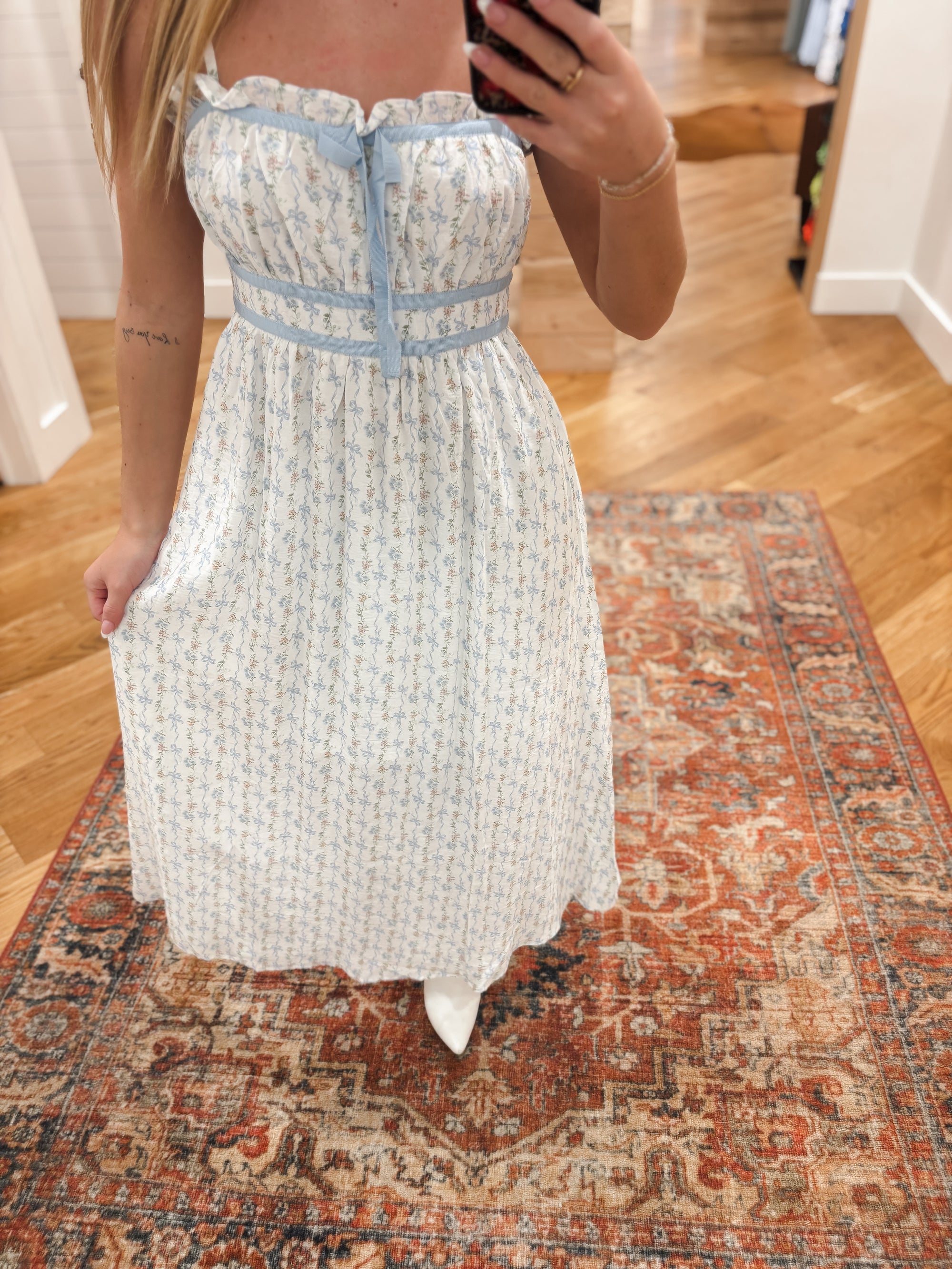 Effortlessly elevate your style with our Calla Blue Midi Dress. Featuring a charming floral bow pattern and ruffle trim, this dress is designed with a square neckline, adjustable spaghetti straps, and an elastic back waist tunnel for a flattering fit. The contrast front tie detail adds a touch of elegance. Boutique style Ashland, Kentucky 